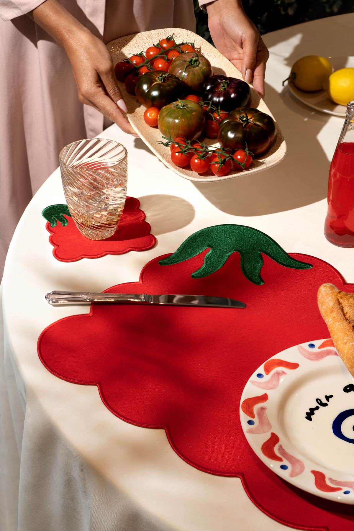 Person holding a plate of assorted tomatoes over a table set with bread, glass, and Octaevo Tomato Coasters (Set of 4).