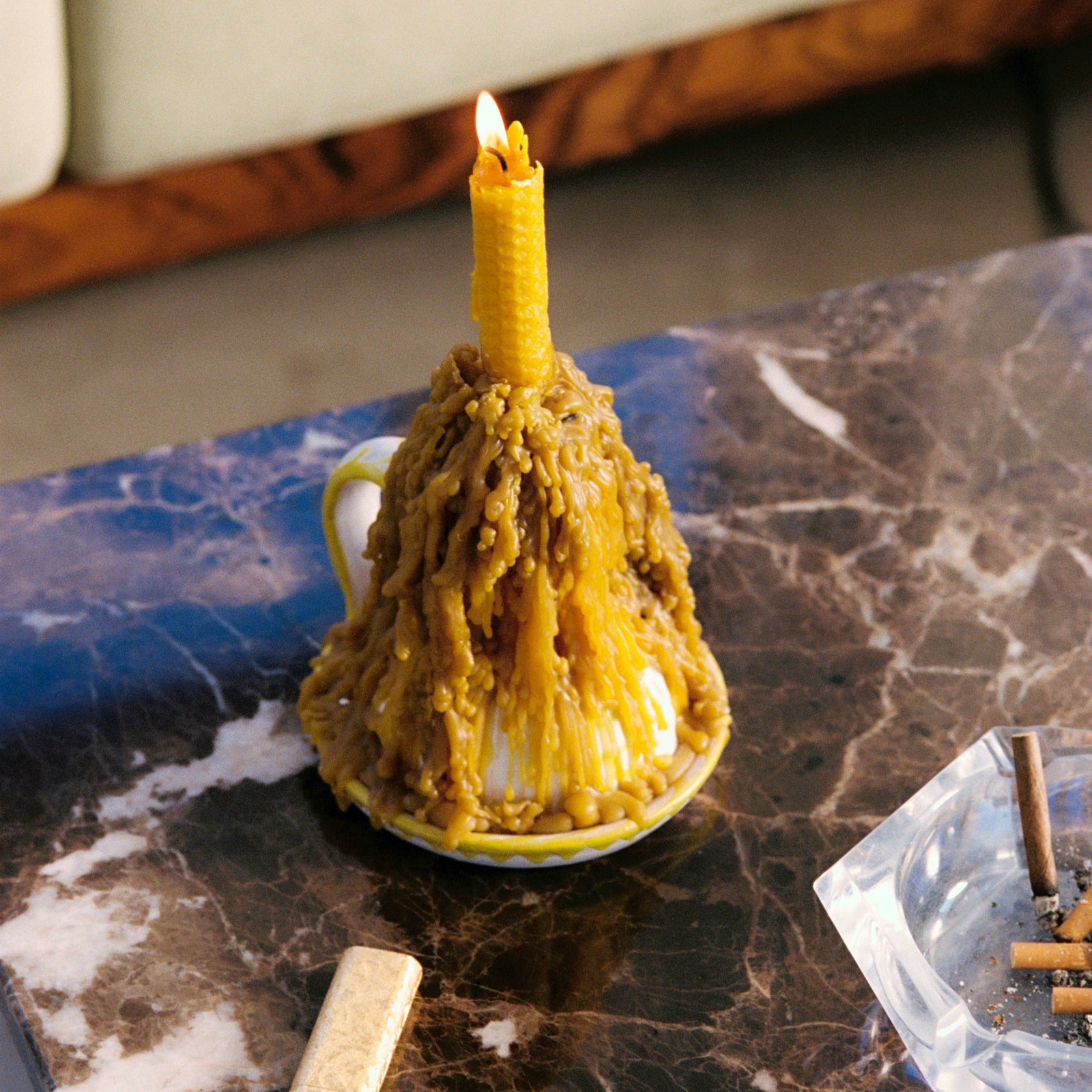 Burnt candle in a white cup on a marble surface with matches and an ashtray. - lifestyle