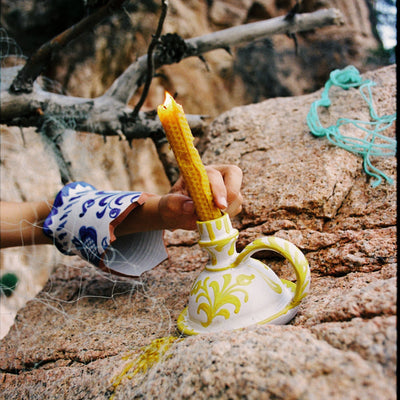 Hand holding a lit candle inside a decorative ceramic holder on a rocky surface with natural background - lifestyle
