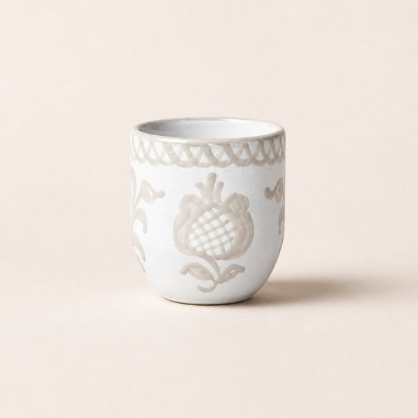 White ceramic cup with decorative patterns on a beige background