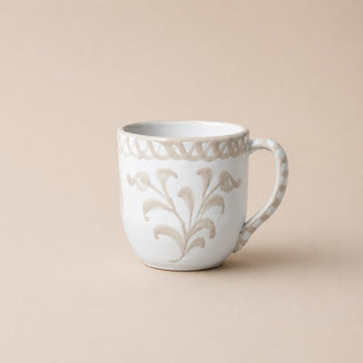 White ceramic mug with decorative floral pattern on a beige background