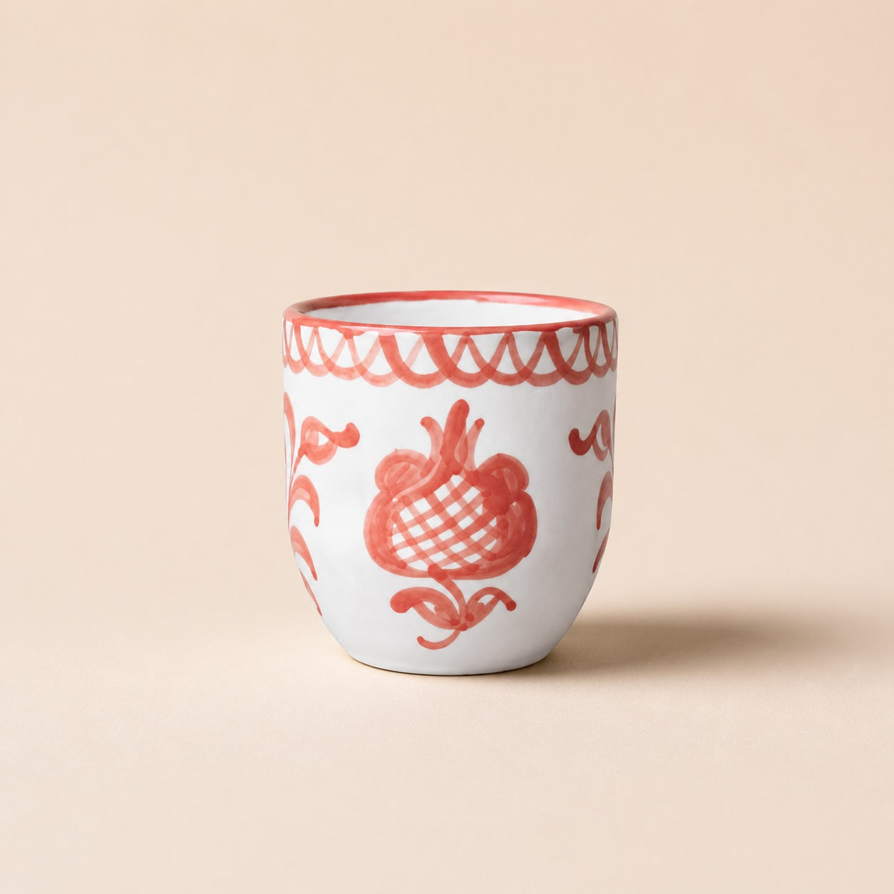 White ceramic cup with red floral patterns on a beige background