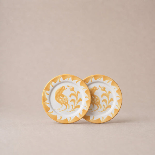 Two ceramic plates with gold and white floral designs on a beige background