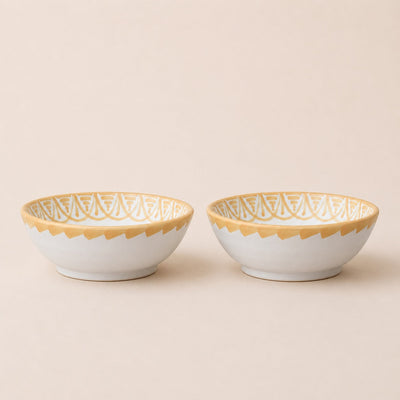 Two ceramic bowls with gold lace patterns on a beige background