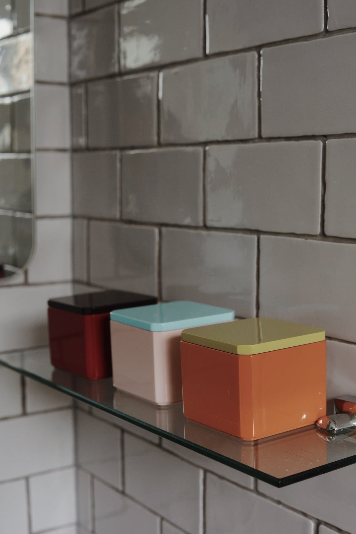 Three colourful high-gloss lacquer trinket boxes on a bathroom shelf, suitable for storing cotton pads, hair ties, jewellery and small everyday essentials.
