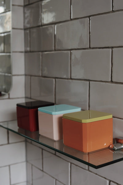 Three colourful high-gloss lacquer trinket boxes on a bathroom shelf, suitable for storing cotton pads, hair ties, jewellery and small everyday essentials.