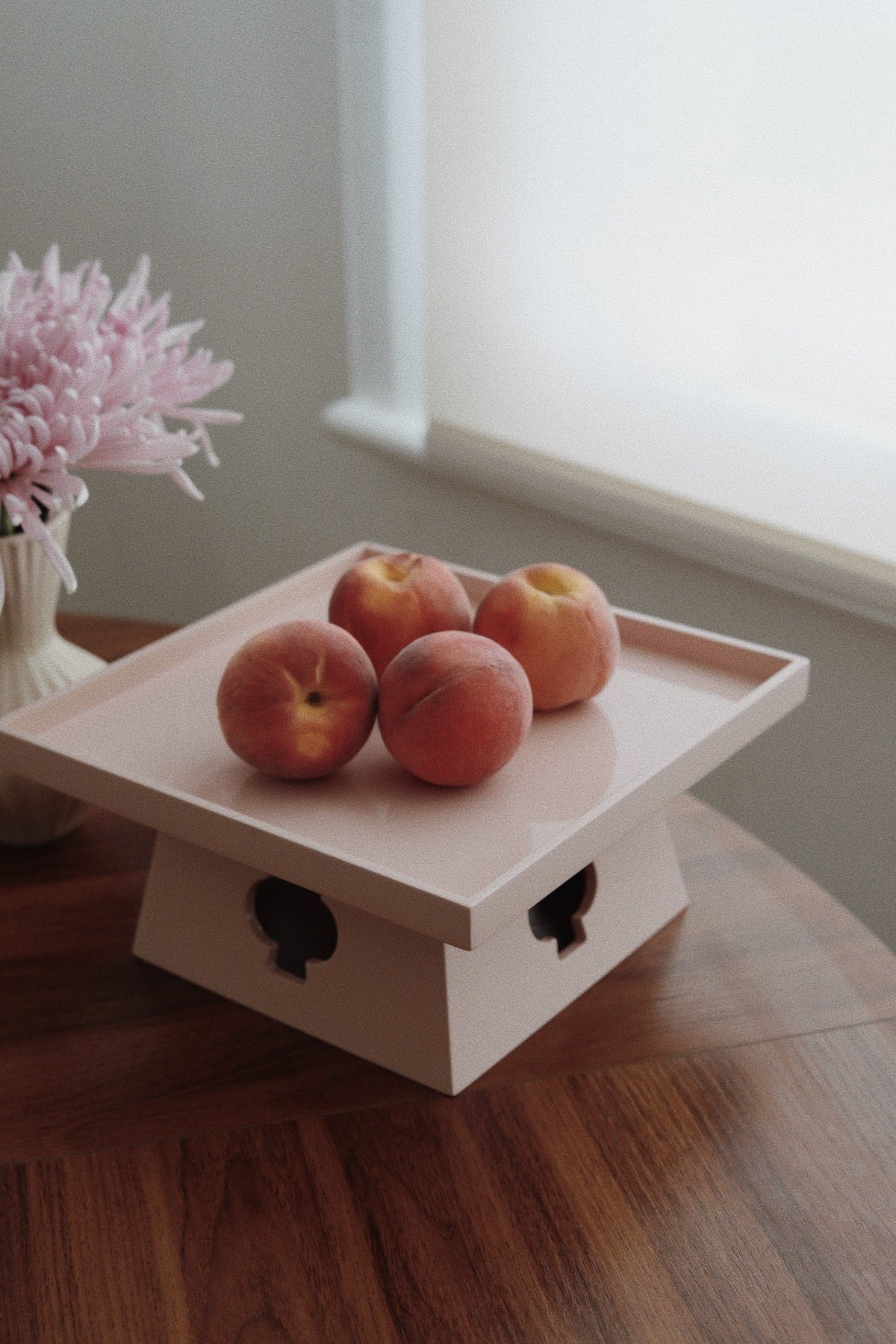 Vinidec peach elevated lacquered pedestal tray styled with fresh peaches on a wooden dining table