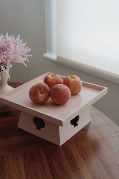 Vinidec peach elevated lacquered pedestal tray styled with fresh peaches on a wooden dining table