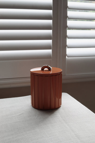 Vinidec fluted lacquer ice bucket in warm burnt amber with a polished chrome arc handle, set against a window with neutral linen for autumn tablescape styling.