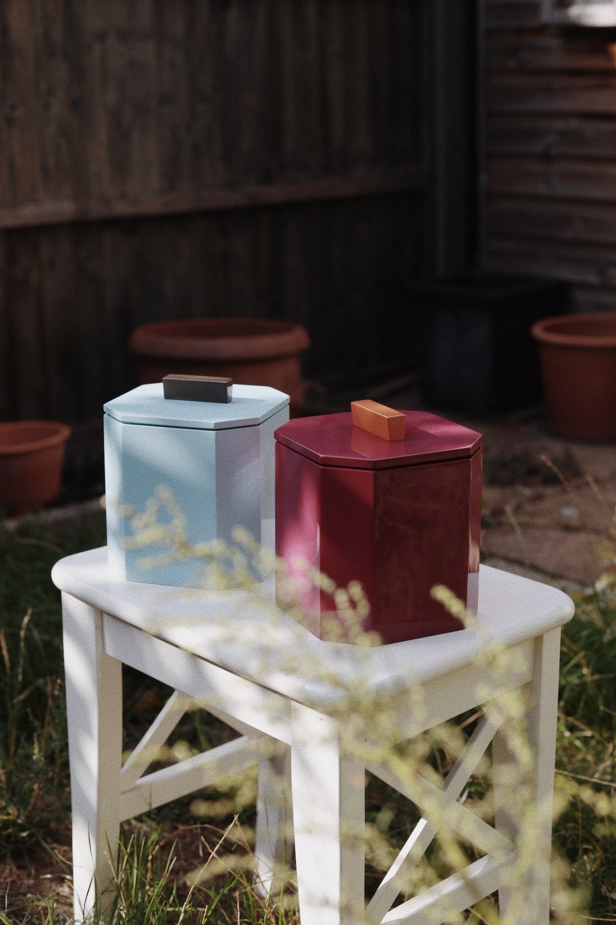 Blue and burgundy VINIDEC lacquer ice buckets displayed outdoors on a white side table.