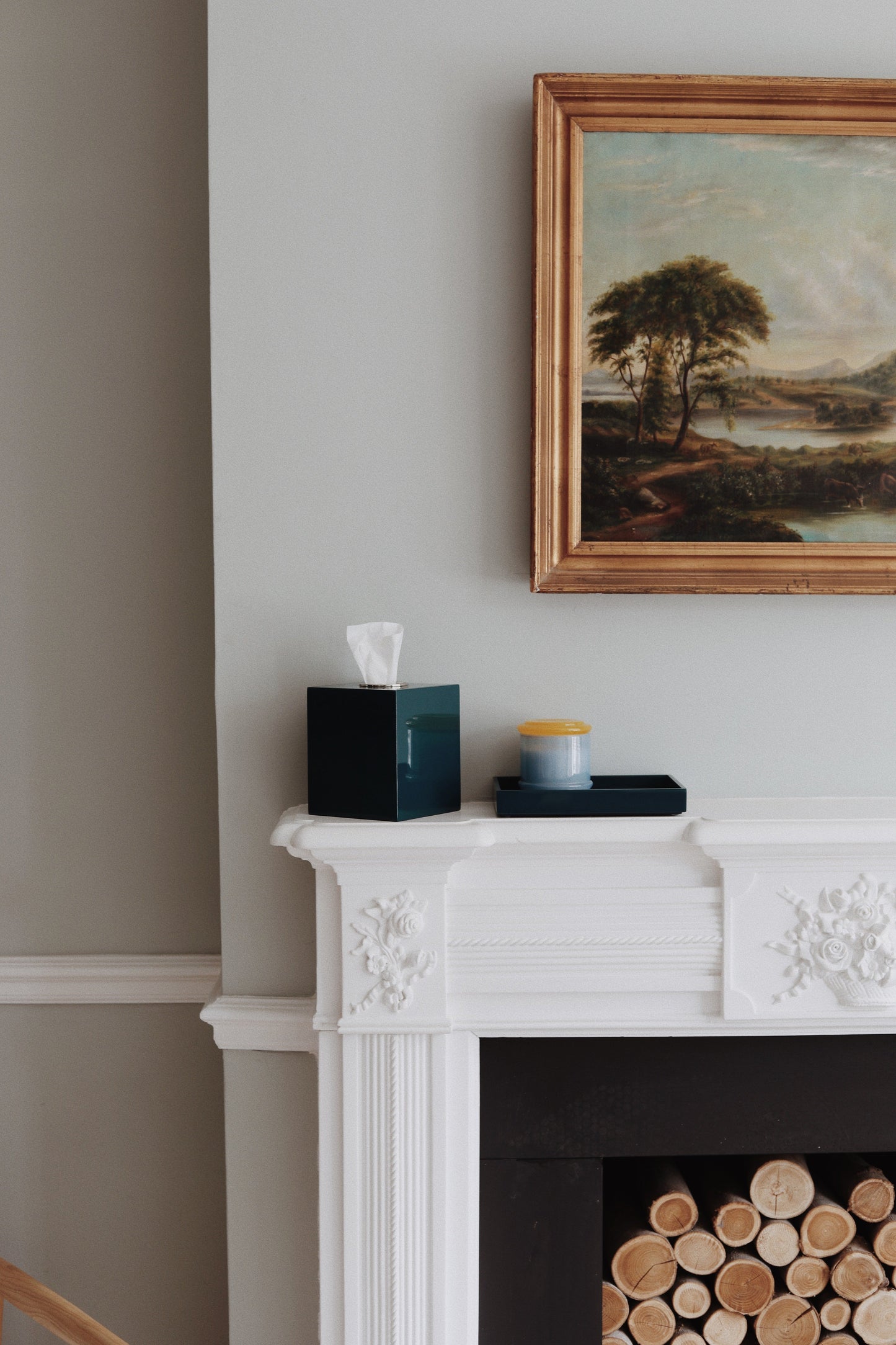 Vinidec linear lacquered tissue box cover in dark teal styled on a white fireplace mantel next to an oil painting. High-gloss homeware. Styling tips for home and interior design. Dark teal lacquer tissue box cover and matching vanity tray styled on a white carved fireplace mantel under an oil painting. Elegant living room fireplace decor ideas by Vinidec.
