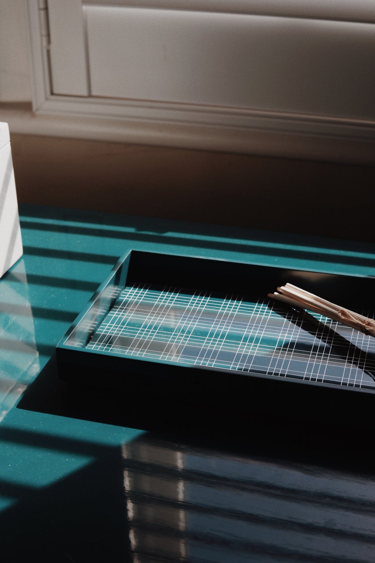Vinidec wide linear lacquered tray in deep teal with geometric white grid pattern lit by slatted window light