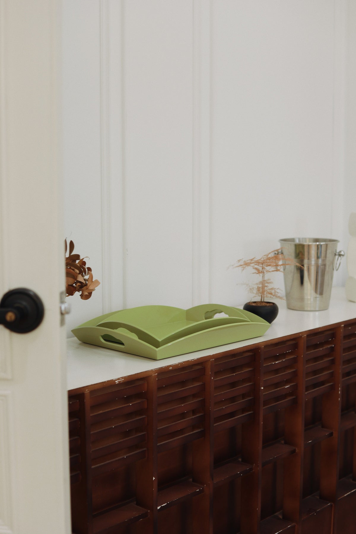 inidec medium curvy serving tray stacked in pistachio green, styled on a wooden sideboard in a bright London interior