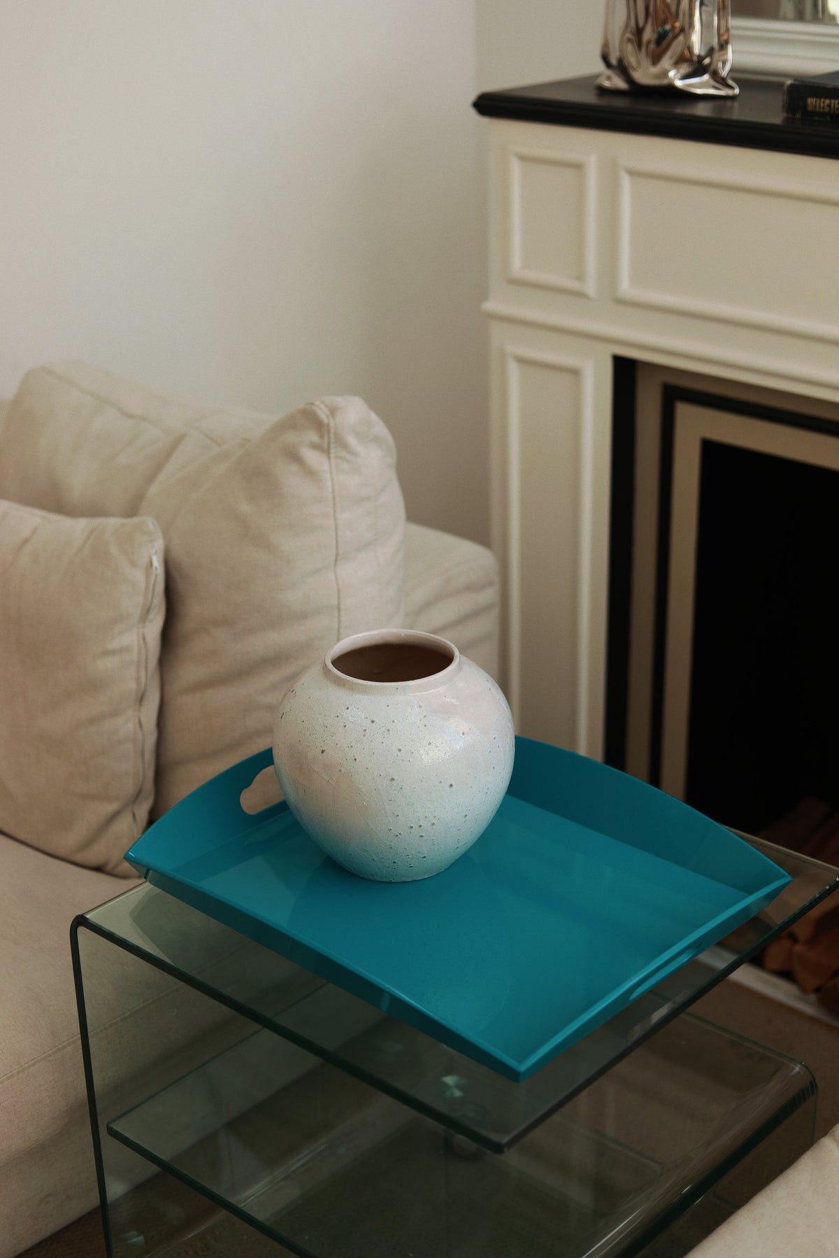 Vinidec medium curvy serving tray in vibrant turquoise blue, styled with a white ceramic vase on a glass side table between armchairs
