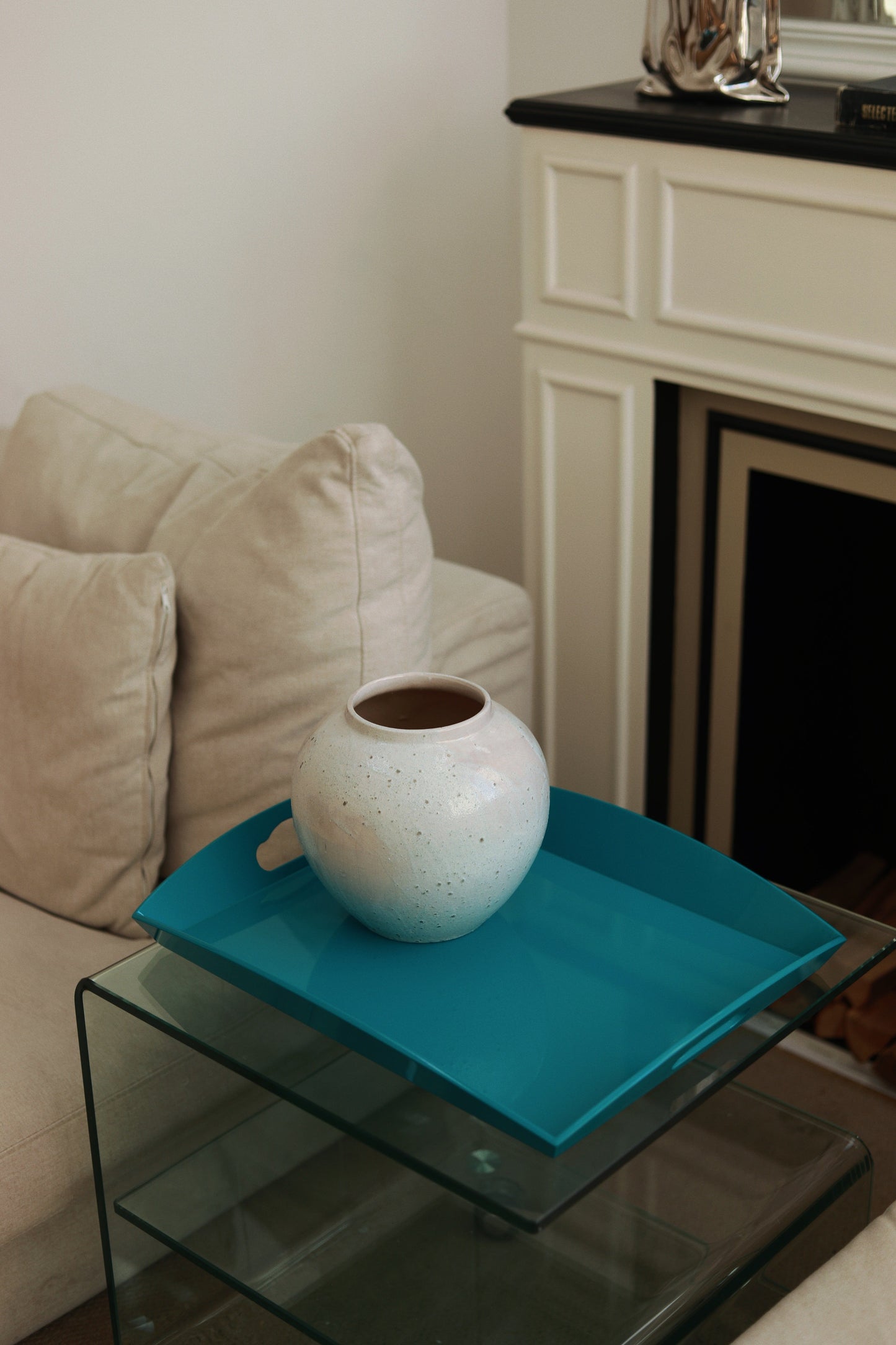 Vinidec medium curvy serving tray in vibrant turquoise blue, styled with a white ceramic vase on a glass side table between armchairs