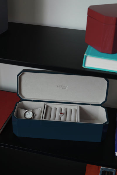Vinidec octagonal jewellery and watch box in open dark blue lacquer, displaying a watch cushion and ring rolls on dark shelving