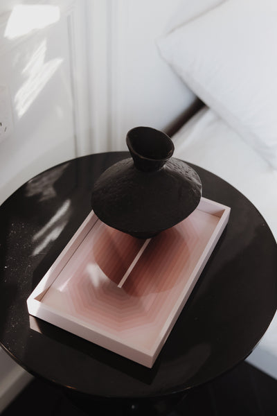 Small sand pink Chiaroscuro high-gloss lacquer tray styled with a black ceramic vase on a bedside side table