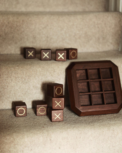 Detail shot of Vinidec walnut wood noughts and crosses blocks with brass O and X inlays stacked beside the octagonal wooden game board