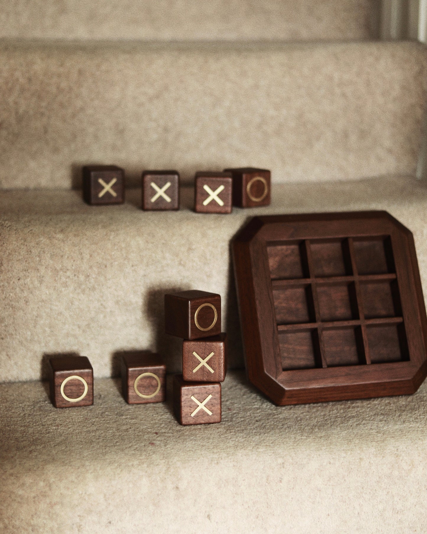Detail shot of Vinidec walnut wood noughts and crosses blocks with brass O and X inlays stacked beside the octagonal wooden game board