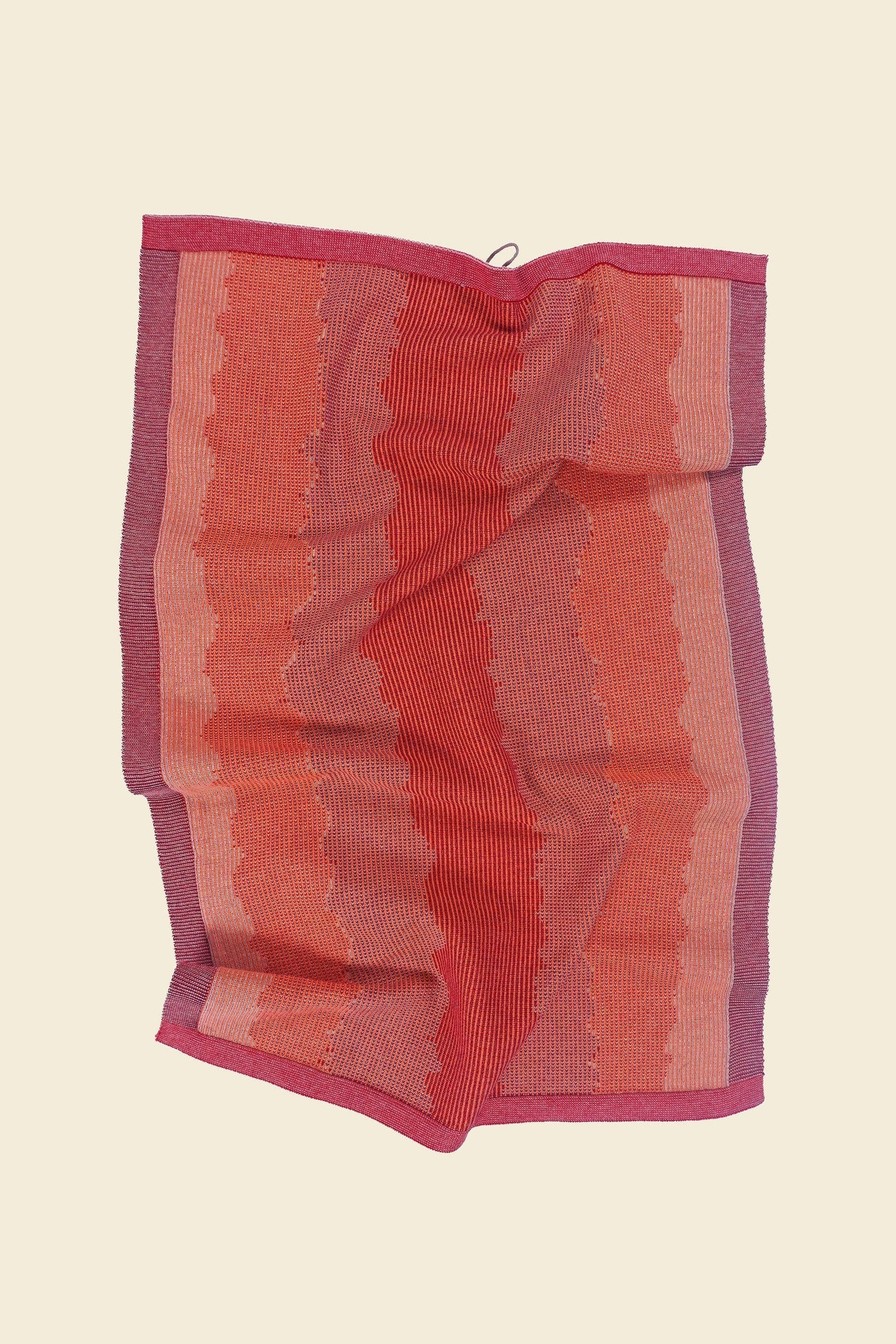 front view of red knit organic cotton kitchen towel with wavy pattern with folds