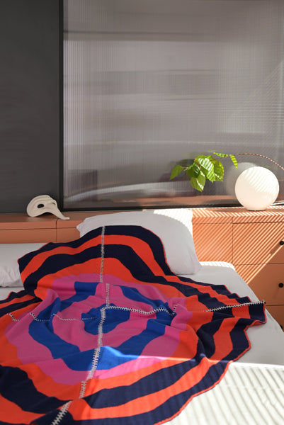 dark wavy knit wool blanket on bed with hand-stitched seam in blue, pink, red and navy 