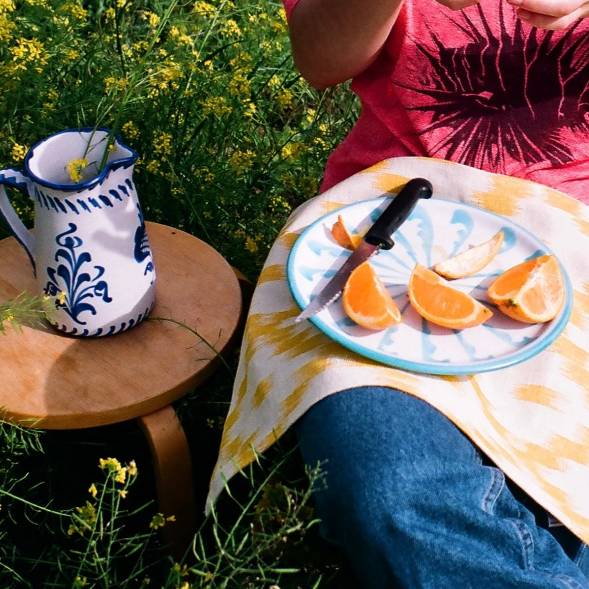 Person sitting outdoors with a plate of oranges and a ceramic pitcher on a grassy background - lifestyle