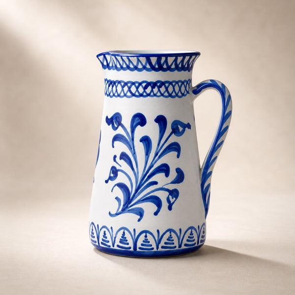 White ceramic pitcher with blue floral patterns on a beige background.