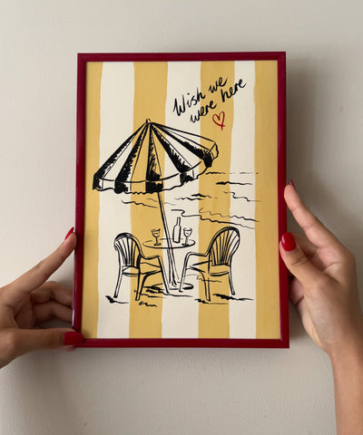 "Wish We Were Here" ink sketch print of a beach parasol and plastic chairs on a striped background, seaside wall art in frame