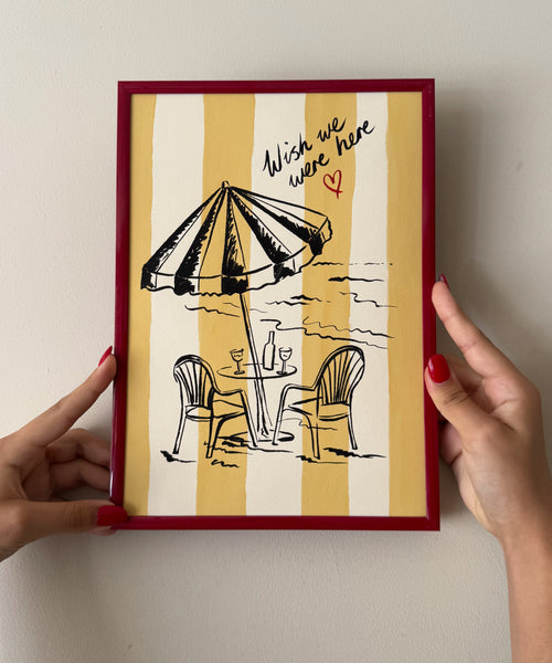 "Wish We Were Here" ink sketch print of a beach parasol and plastic chairs on a striped background, seaside wall art in frame