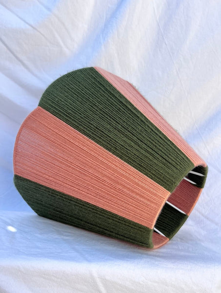 A slice shades handwoven striped scallop yarn lampshade in olive green and plaster pink with white background.